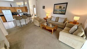 A living room with a sofa, a coffee table, and a painting of a beach scene. - Charming Pool Home, with game room. 15 minutes from Disney parks. (Davenport)