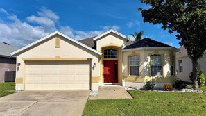 A residential house with a garage, a red door, and a small attached structure with windows.