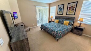 A bedroom with a bed, two bedside tables, a nightstand, a dresser, a mirror, and a window with blinds.
