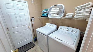 A laundry room with two white front-loading washing machines, a shelf with folded towels, and a door. - Envious Highlands Reserve pool home with recent upgrades. (Davenport)