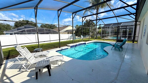 A covered outdoor swimming pool with lounge chairs and a white fence in the background.