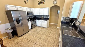 A kitchen with white cabinets, a stainless steel refrigerator, a microwave, and a tiled backsplash. - Stunning, large Highlands Reserve with game room and pool! (Davenport)