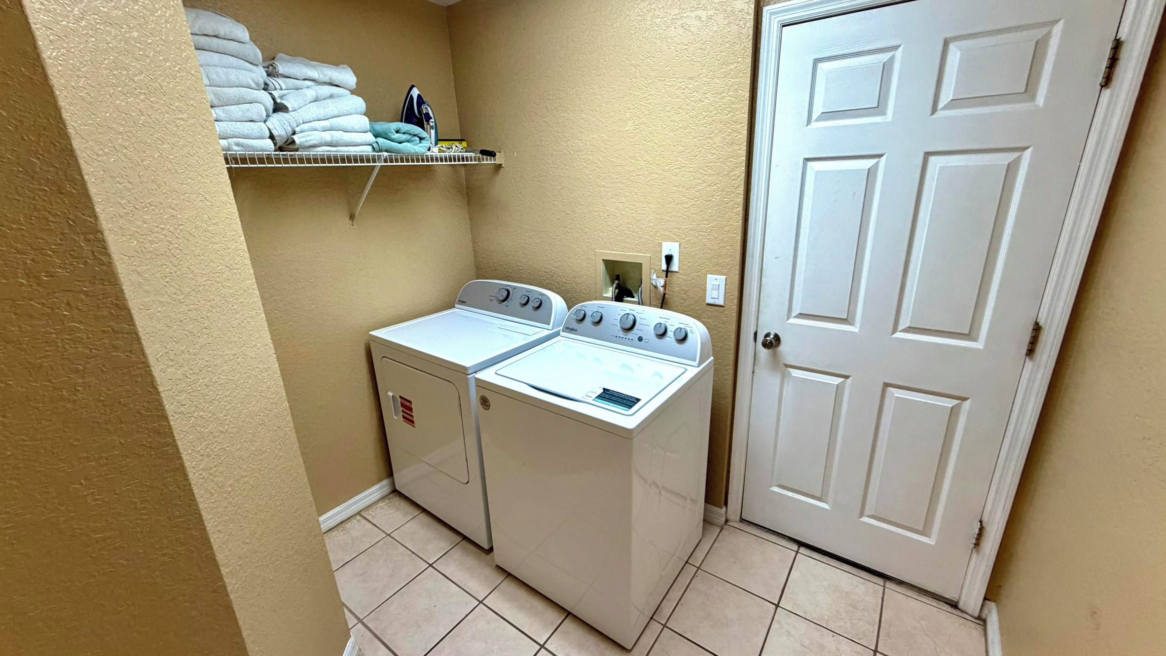 A laundry area with two washing machines, a shelf with folded towels, and a closed door.