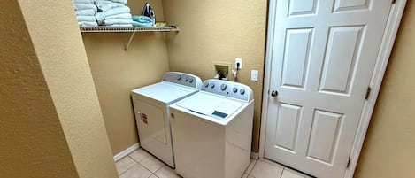 A laundry area with two washing machines, a shelf with folded towels, and a closed door.
