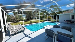 A covered outdoor swimming pool with lounge chairs and a table.