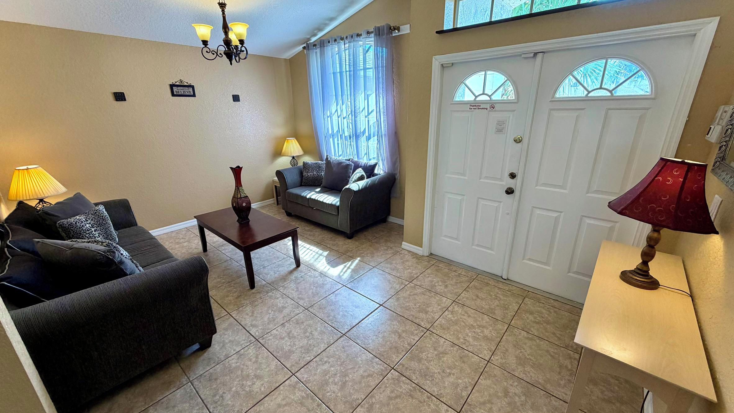 A living room with a sofa, coffee table, and lamps. There is a door with a window and a sign above it.