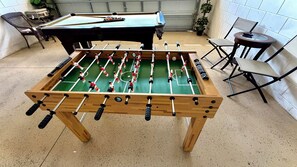 Ein Kicker steht in einem Raum mit Billardtisch, Stühlen und einem kleinen Tisch.
