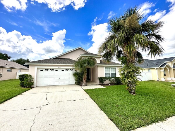 A single-story house with a white garage, a well-maintained lawn, and a palm tree. - Family time, quiet relaxation, Florida fun. Pool Home at Orange Tree (Clermont)