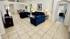 A spacious living room with a high ceiling, a ceiling fan, and a dining area with chairs and a table.