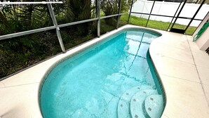 A swimming pool with a curved edge, surrounded by a tiled deck and a metal fence.