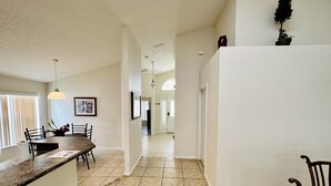 A spacious kitchen with a central island, a dining area with chairs, and a hallway leading to other rooms.