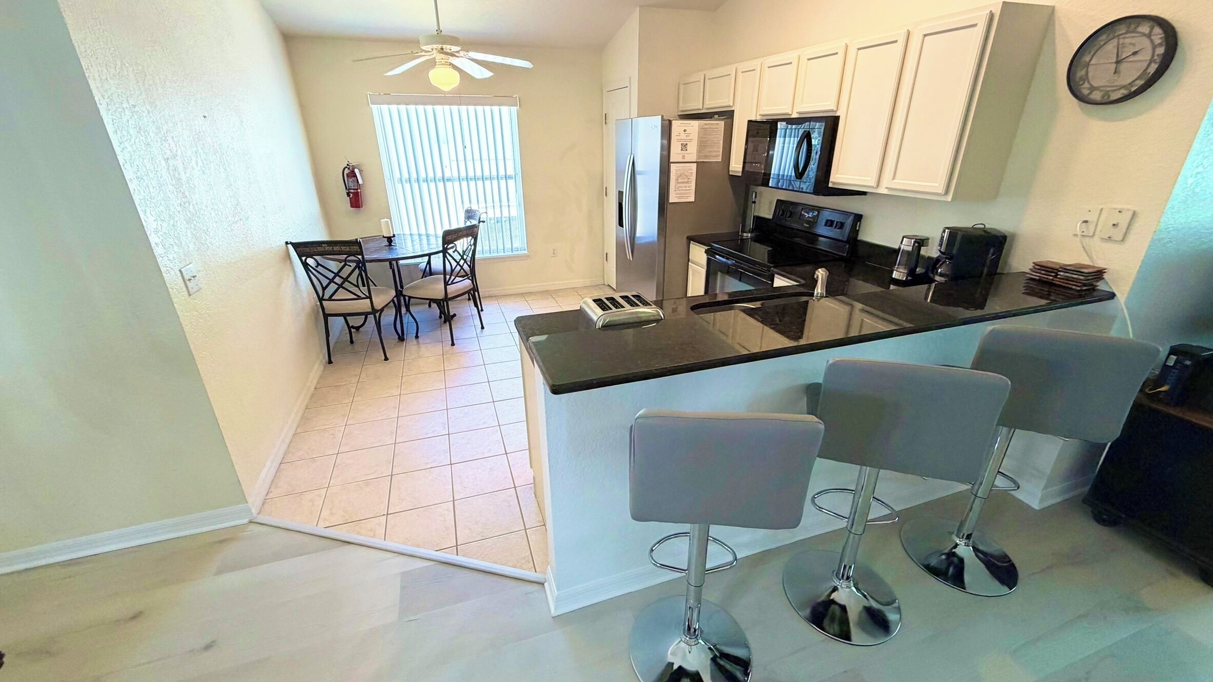 A kitchen with a central island, bar stools, a refrigerator, a microwave, and a dining area with chairs.