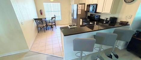 A kitchen with a central island, bar stools, a refrigerator, a microwave, and a dining area with chairs.