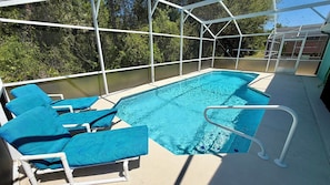 A swimming pool with blue lounge chairs and a white safety railing.
