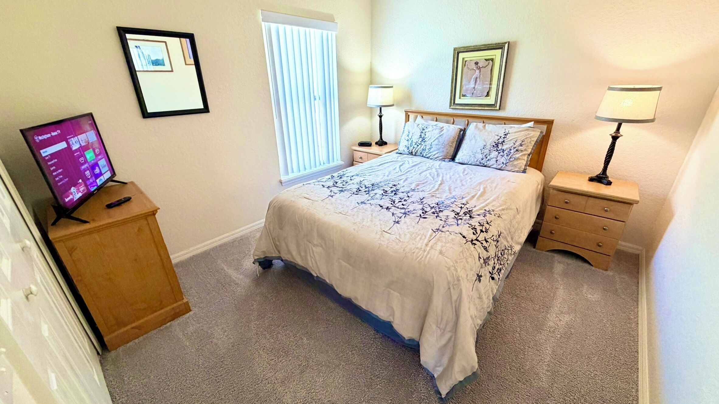 Un dormitorio con una cama, dos mesitas de noche con lámparas, un televisor sobre un mueble bajo y cuadros enmarcados en las paredes.