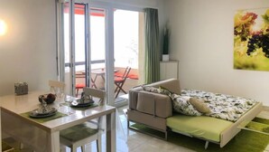 Een moderne woonkamer met een bank, een eettafel met stoelen en een schuifpui naar een terras.