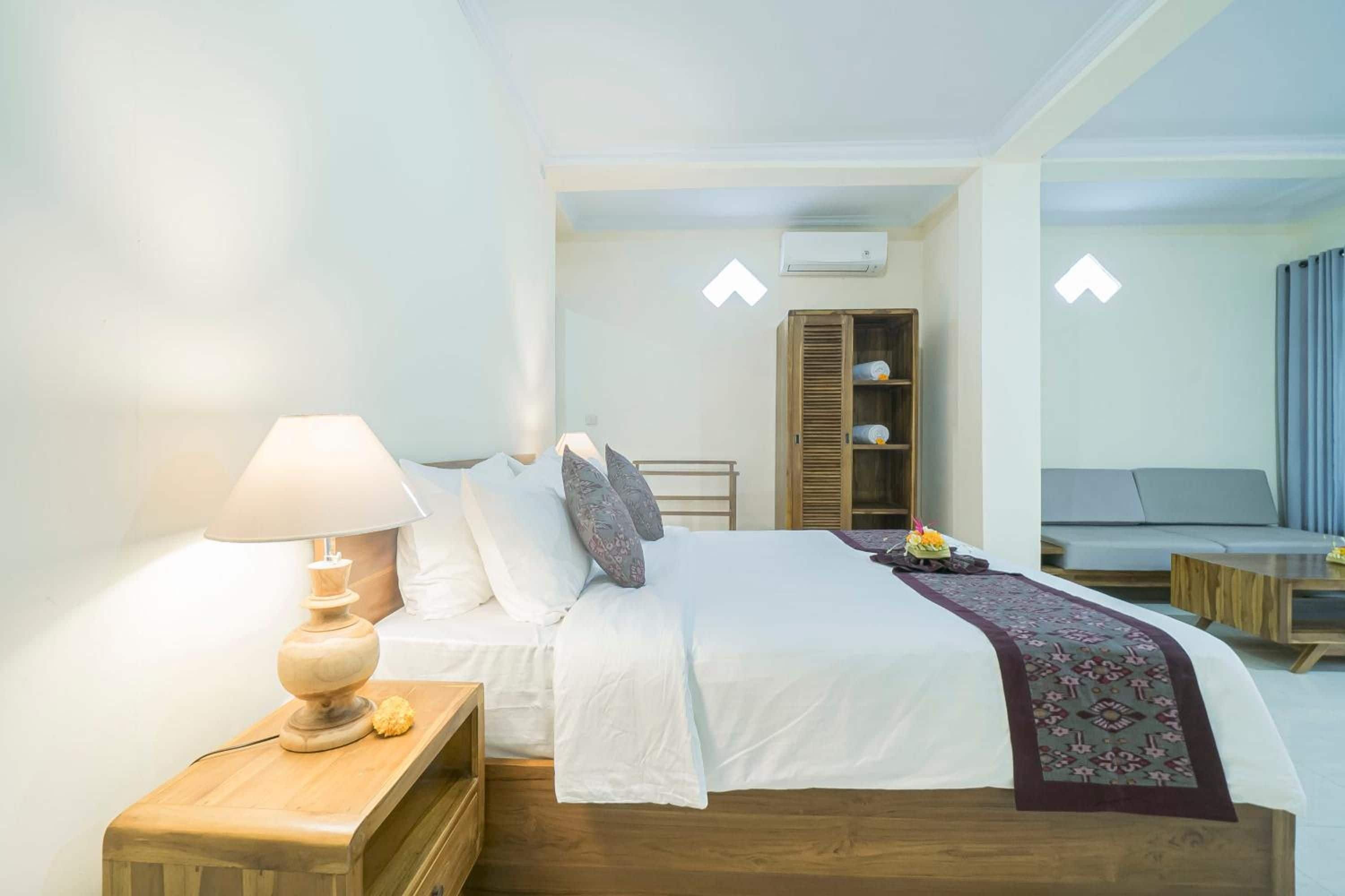 Habitación de hotel con cama, mesita de noche, lámpara, armario y zona de estar con sofá y mesa de centro.