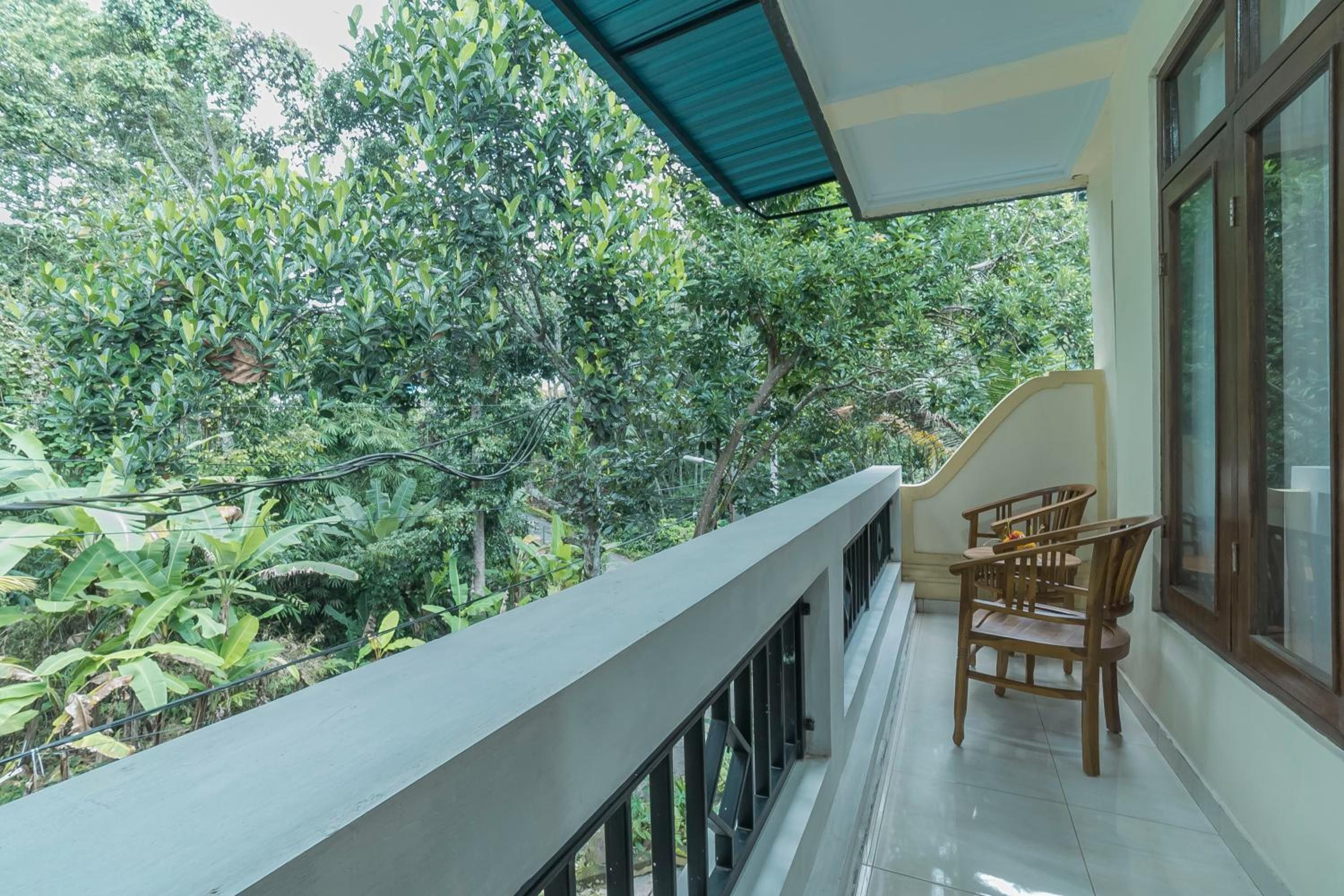 A balcony with a view of dense foliage, a tiled floor, and wooden chairs.