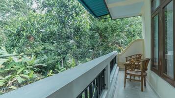 A balcony with a view of dense foliage, a tiled floor, and wooden chairs.