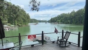 Eine Holzterrasse mit einem Schild 'No Diving Shallow Pool', die auf einen ruhigen Fluss mit Booten und einer an einem Steg liegenden Schiffahrt blickt.