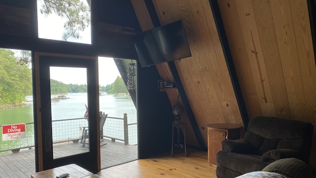 Ein Zimmer mit Holzboden, Blick auf einen See, einem Esstisch und einem Sofa.