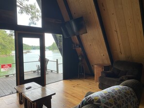A room with a wooden ceiling, a view of a lake, a dining table, a sofa, and a sign indicating no diving in the shallow pool.