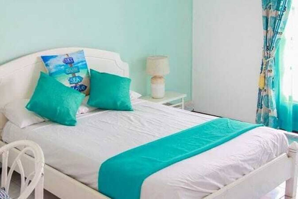 A bed with white bedding and teal accents, a bedside table with a lamp, and a window with curtains.