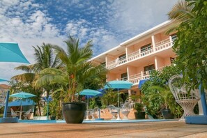 A hotel courtyard with outdoor seating, palm trees, and a two-story building with balconies. - Le Palms Tree Garden Hôtel & Spa (Flic-en-Flac)