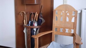 A wooden chair with a decorative backrest and a wooden umbrella stand holding several umbrellas. - Atelier 2 - Atelierhaus Tannenweg (Worpswede)