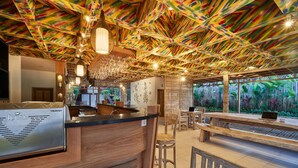 Eine Bar mit einer Holztheke, Barhocker und einer Decke mit bunten Mustern.