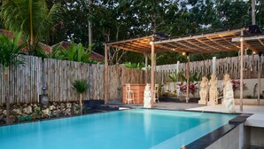 Ein Schwimmbad mit einer Holzterrasse und einem überdachten Sitzbereich.