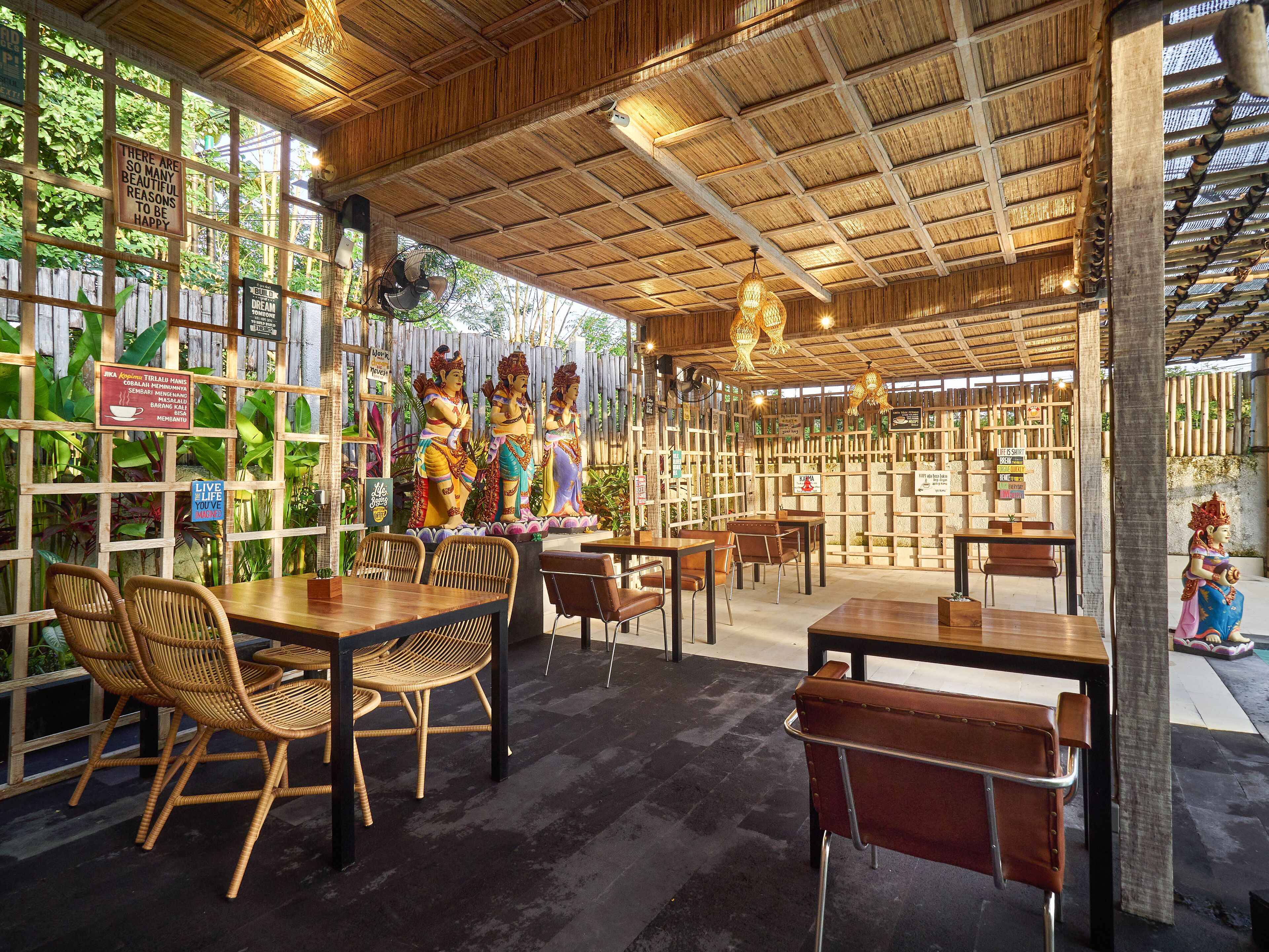 Un restaurante interior con techo de bambú, muebles de madera y estatuas decorativas.