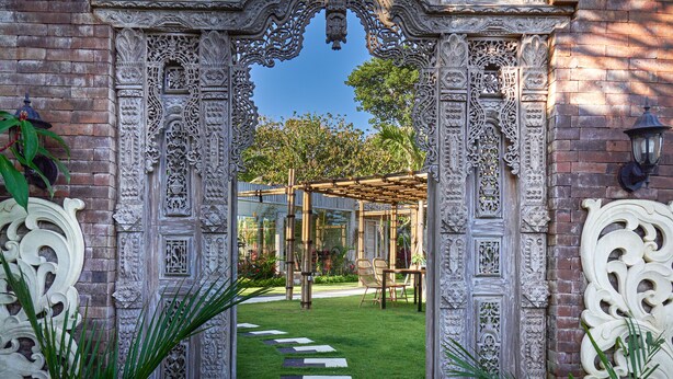 Ein verziertes Tor führt in einen Garten mit einer Pergola und einem Weg.