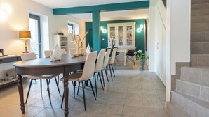 A dining area with a round table and chairs, a cabinet with glass doors, and a staircase. - Gîte Godchure Côté Spa (Saint-Hubert)