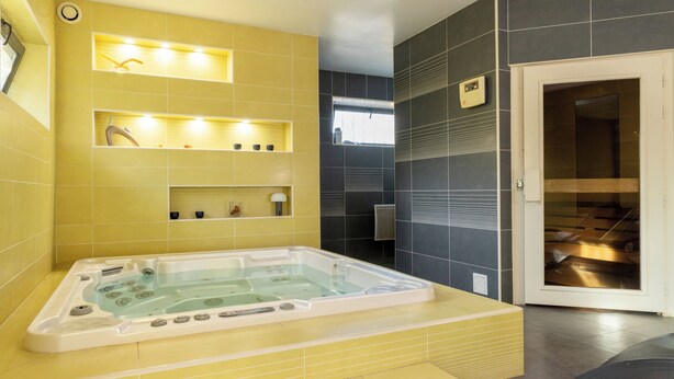 A modern bathroom with a large bathtub, yellow and gray tiled walls, and a glass shower enclosure. - Gîte Godchure Côté Spa (Saint-Hubert)