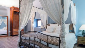 A four-poster bed with a canopy, a wooden wardrobe, a bedside table with a lamp, and a window with curtains. - Gîte Godchure Côté Spa (Saint-Hubert)