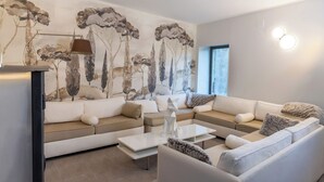 A modern living room with a sectional sofa, a coffee table, and a wall mural. - Gîte Godchure Côté Spa (Saint-Hubert)