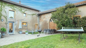 A courtyard with a barbecue grill, outdoor seating, and potted plants. - Gîte Godchure Côté Spa (Saint-Hubert)
