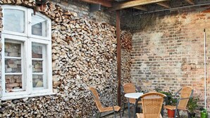Un patio con sillas de mimbre y una mesa, un muro de ladrillo y una ventana con fachada de piedra.