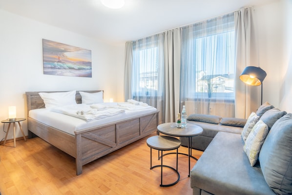 A modern hotel room with a wooden bed, a sofa, a small round table, and a painting on the wall.