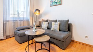 Ein modernes Wohnzimmer mit einem grauen Sofa, zwei runden Tischen, einer Stehlampe und einem Gemälde an der Wand.