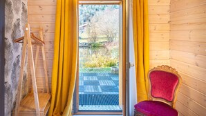 A wooden cabin interior with a door leading to a balcony, a red chair, and a wooden easel.
