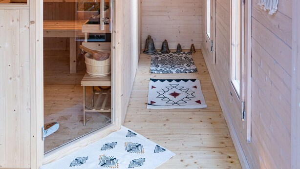 A wooden sauna room with benches, a wooden bench with a towel, and a patterned rug on the floor.