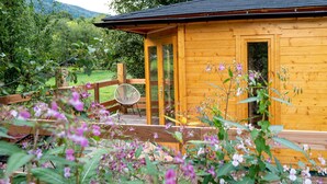 A wooden cabin with a deck, surrounded by lush greenery and flowers.