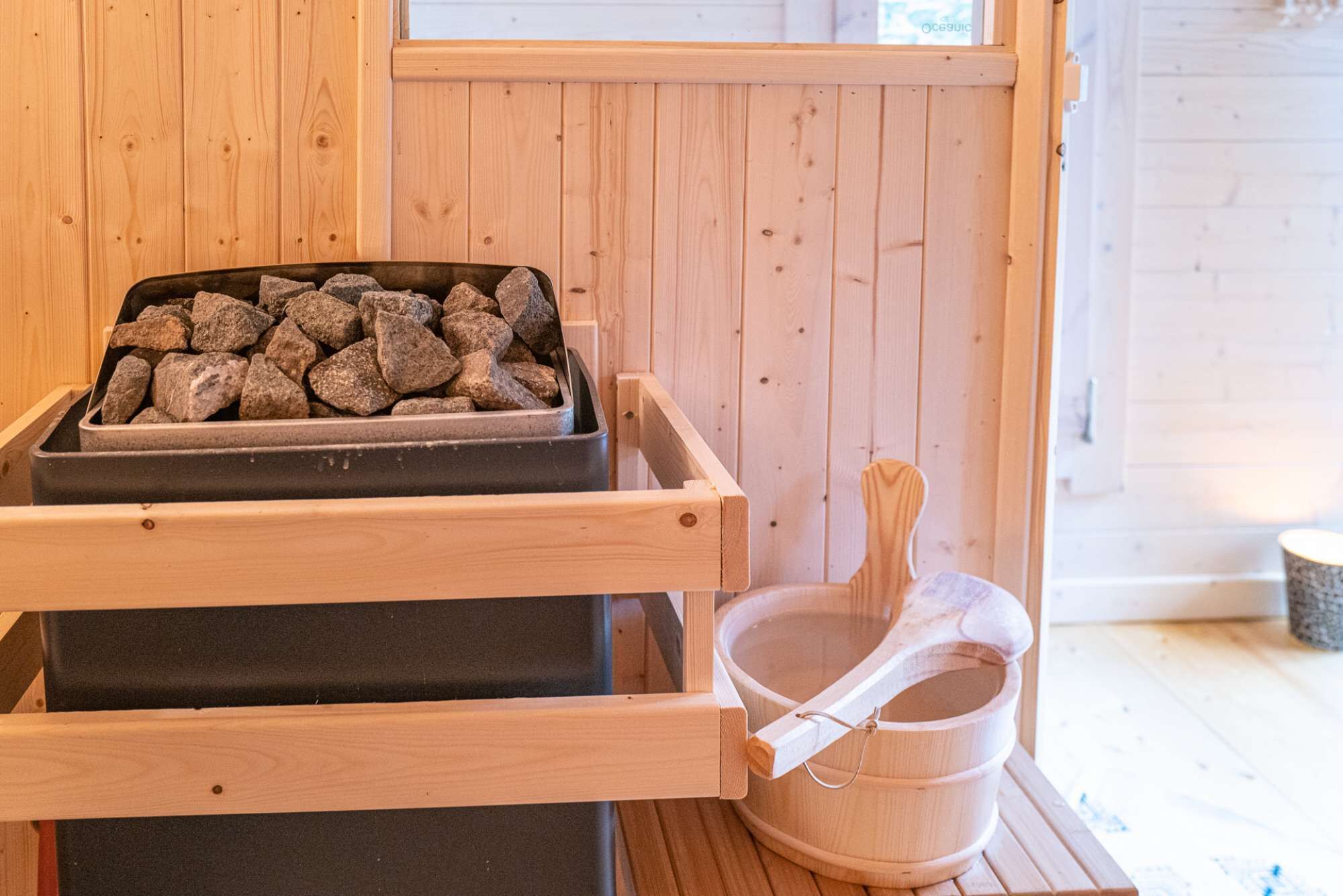 A sauna with a wooden bench, a stone tray, and a wooden bucket.