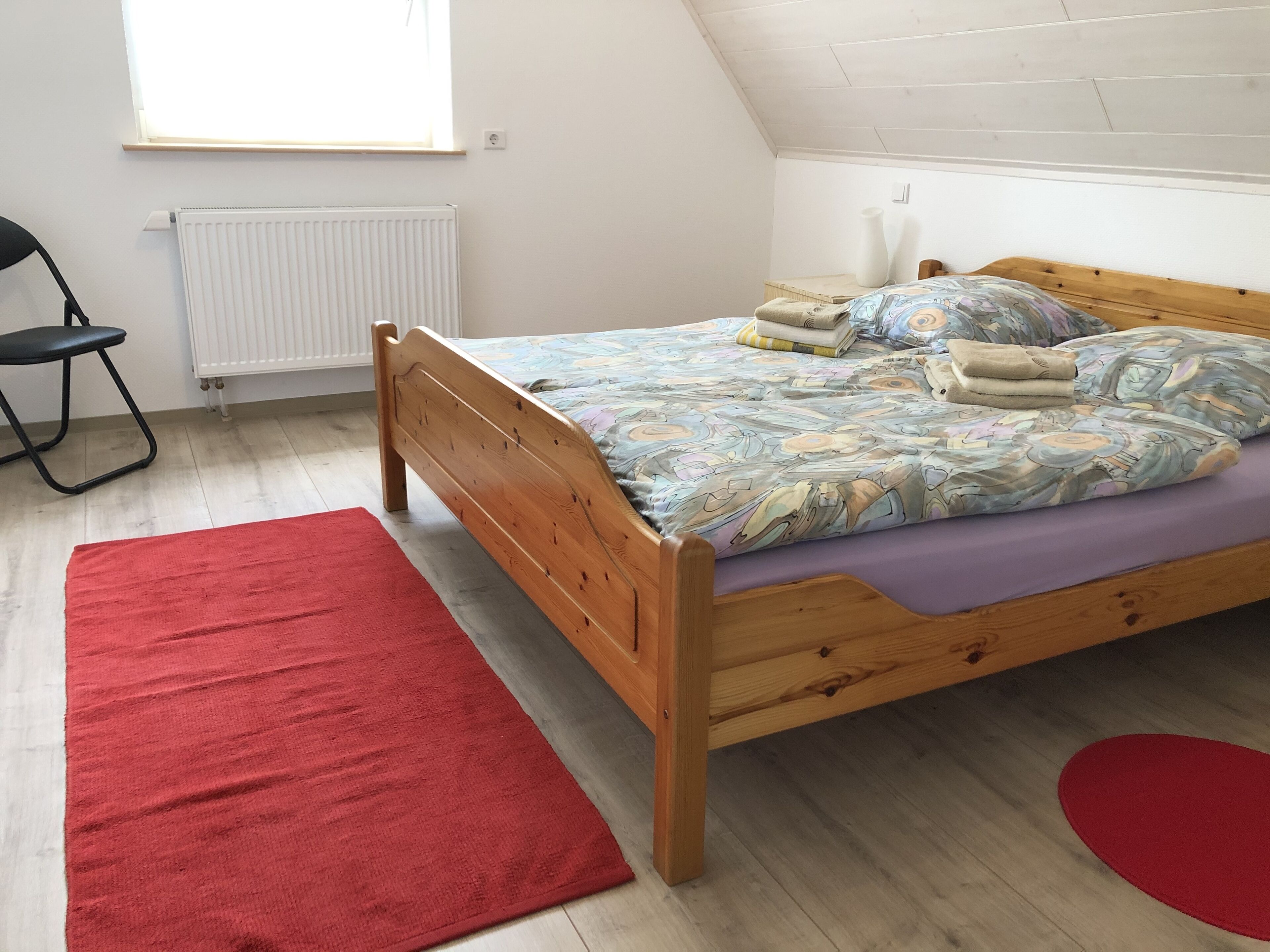 A bedroom with a wooden bed, a red rug, and a window with blinds.