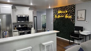 A modern kitchen with white cabinetry, stainless steel appliances, and a neon sign on the wall.