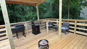 An outdoor deck with a grill, two wicker chairs, and a fire pit.