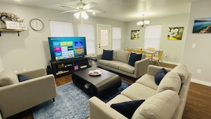A living room with a flat-screen TV, two sofas, a coffee table, and a dining area with a table and chairs.