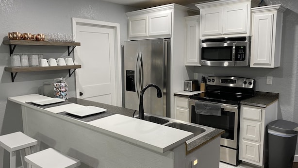 A modern kitchen with white cabinetry, stainless steel appliances, and a central island with a sink.